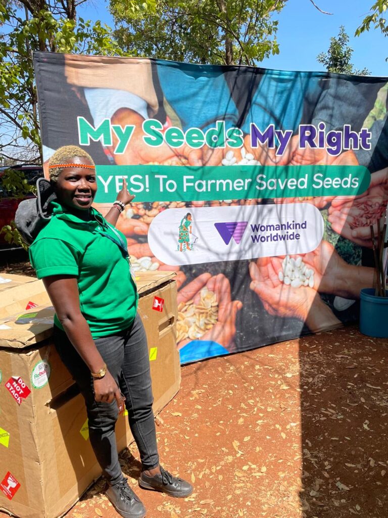 Judy Kipkenda of Koibatek Ogiek Women and Youth Network standing next to a banner written My Seed, My Right in Zimbabwe.
